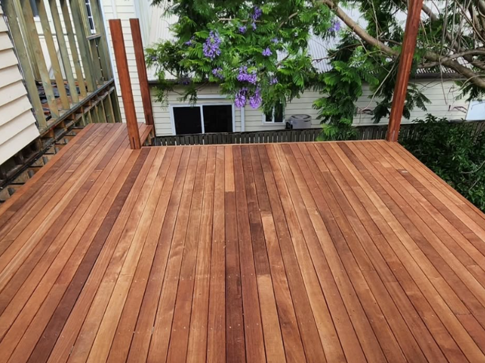 A newly finished hardwood deck with a garden behind it