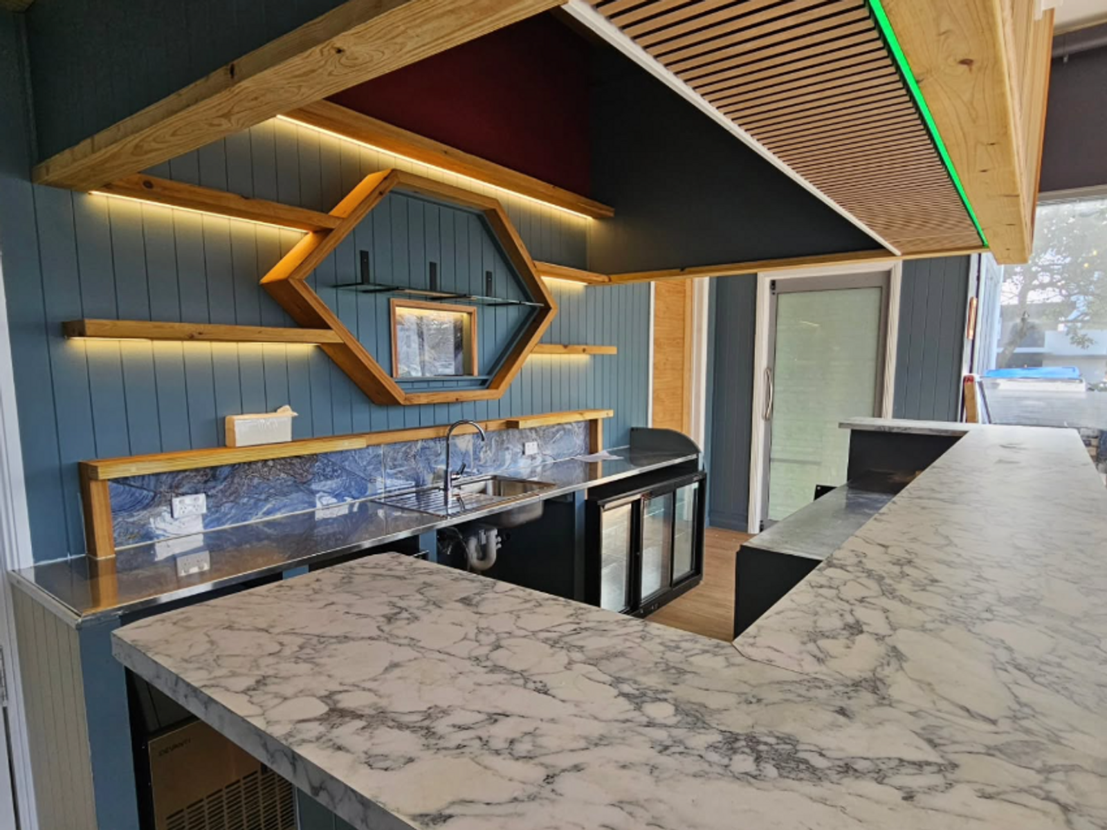 A timber lined shop fitout with a feature hexagonal shelf and stone counter, built by J. Davy Build